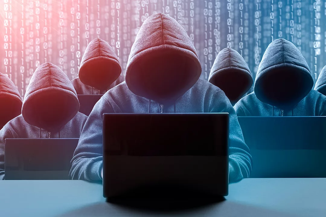 SEVEN HOODED FIGURES, WHOSE FACES CANNOT BE SEEN, ARE SITTING IN FRONT OF LAPTOPS WITH DIGITAL BINARY IN THE BACKGROUND.