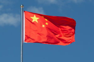 THE CHINESE FLAG IS WAVING IN THE WIND IN FRONT OF A BLUE SKY