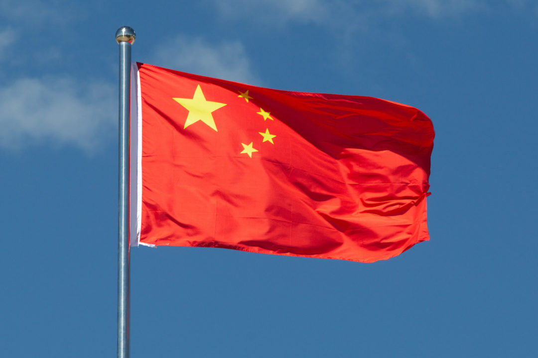 THE CHINESE FLAG IS WAVING IN THE WIND IN FRONT OF A BLUE SKY