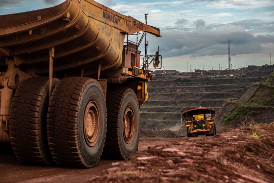 TWO YELLOW HAUL TRUCKS CAN BE SEEN WORKING IN AN IRON ORE MINE.
