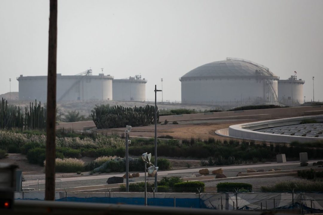 THREE LARGE WHITE OIL STORAGE TANKS CAN BE SEEN NEAR A HIGHWAY SURROUNDED BY ROLLING FIELDS.