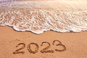 A WAVE APPROACHES A SANDY BEACH WITH THE NUMBER "2023" DRAWN IN THE SAND