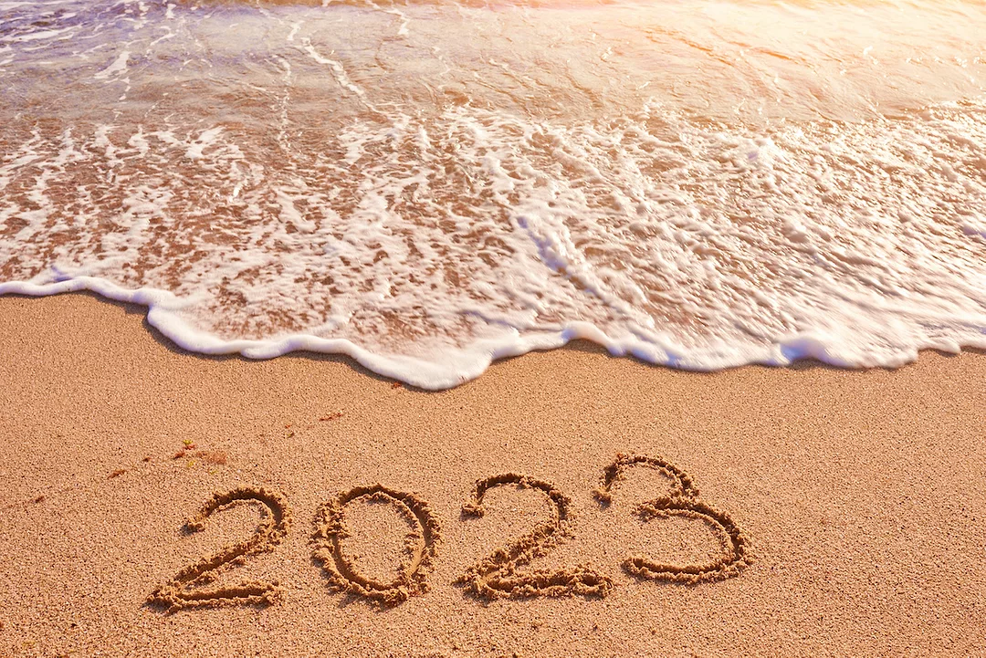 A WAVE APPROACHES A SANDY BEACH WITH THE NUMBER "2023" DRAWN IN THE SAND
