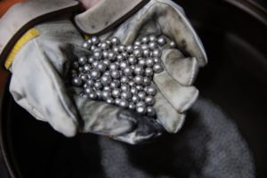 A PAIR OF HANDS WEARING THICK WORK GLOVES CAN BE SEEN HOLDING MANY SMALL BALLS OF NICKEL.