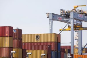 A STACK OF CONTAINERS STANDS IN FRONT OF A CRANE AT A PORT