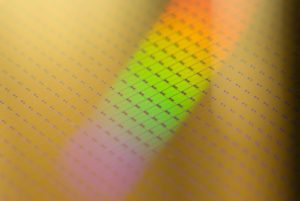 THE SURFACE DETAILS OF A FAB 11 SILICON SEMICONDUCTOR CAN BE SEEN. A RAINBOW IS REFLECTED ON THE MOSTLY YELLOW SURFACE.