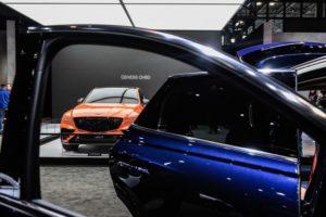 THE OPEN DOORS OF A BLUE HYUNDAI VEHICLE CAN BE SEEN. AN ORANGE HYUNDAI CAN BE SEEN IN THE BACKGROUND THROUGH THE OPEN WINDOW PASSENGER-SIDE WINDOW OF THE BLUE CAR IN THE FRONT.