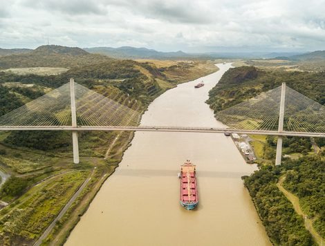 A SHIP LOADED WITH ORANGE CONTAINERS MAKES WAY UNDER A BRIDGE OVER A MUDDY BROWN WATERWAY