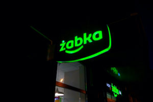 A BLACK AND GREEN ŻABKA SIGN IS ILLUMINATED AT NIGHT OUTSIDE OF A STORE.
