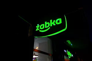 A BLACK AND GREEN ŻABKA SIGN IS ILLUMINATED AT NIGHT OUTSIDE OF A STORE.
