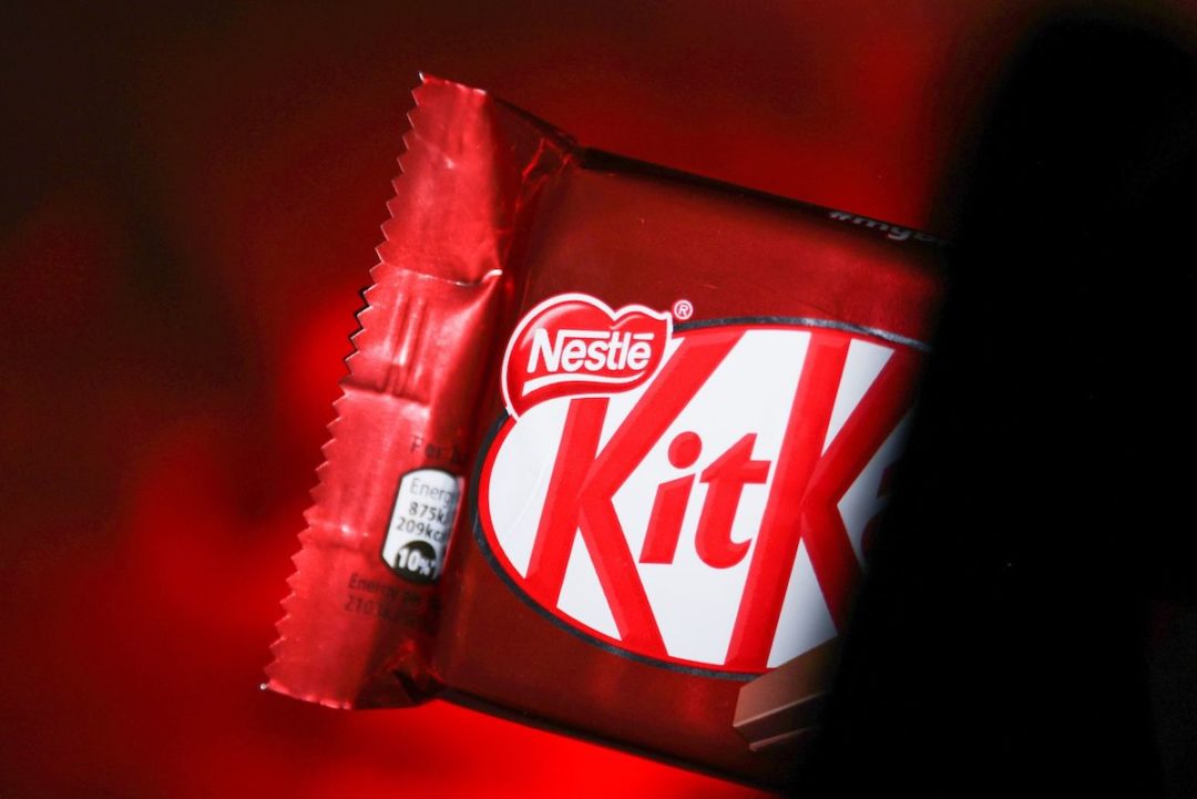 THE OUTSIDE OF A KITKAT WRAPPER CAN BE SEEN IN FRONT OF A RED BACKGROUND.
