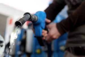 A PERSON IS USING THEIR HANDS TO GRIP A BLUE GASOLINE PUMP WHILE GASOLINE COMES OUT OF THE PUMP'S NOZZLE.