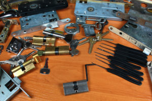 SEVERAL LOCKS, LOCK-PICKING TOOLS, KEYS, AND OTHER LOCK-RELATED PRODUCTS SIT ON TOP OF WHAT APPEARS TO BE A WOODEN DESK.