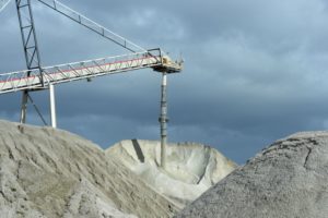 A CRANE WITH A TUBE ATTACHED DELVES INTO A GIANT MOUND OF WHITISH POWDER