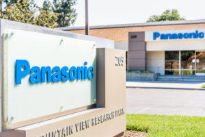 A PANASONIC SIGN SITS IN A SMALL PATCH OF GRASS IN SILICON VALLEY WITH A PANASONIC BUILDING IN THE BACKGROUND OF THE IMAGE.