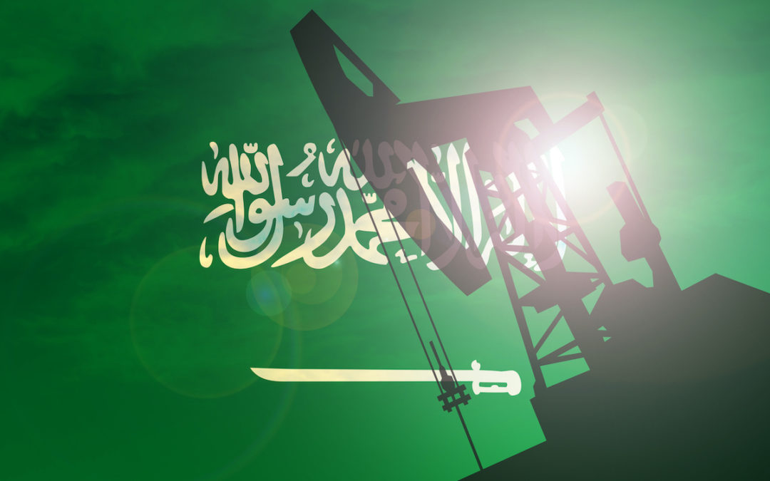 AN OIL PUMP CAN BE SEEN WITH THE SUN SHINING ON IT IN FRONT OF THE SAUDI ARABIAN FLAG.