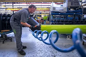 A FACTORY WORKER CAN BE SEEN HOLDING A DEVICE WITH A LONG SPIRALING BLUE TUBE ATTACHED TO THE END OF IT.