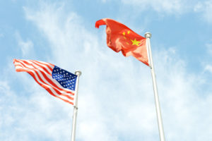 A LOOKING UP VIEW OF THE U.S. AND CHINESE FLAGS WAVING IN FRONT OF A BLUE SKY.