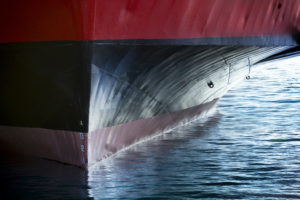 THE BOW OF A LARGE TANKER SHIP CAN BE SEEN IN A BODY OF WATER. THE BOW IS RED ON TOP AND BLACK ON THE BOTTOM.