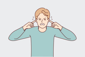 AN ILLUSTRATION DEPICTS AN UNHAPPY MAN WITH HIS EYES CLOSED PLUGGING HIS EARS WITH HIS INDEX FINGERS.