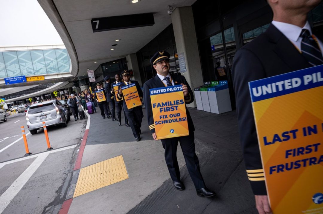 UNIFORMED PILOTS OUTSIDE AN AIRPORT BEAR SIGNS THAT READ "FAMILY FIRST"