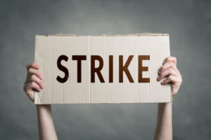 A PAIR OF HANDS HOLDS A SIGN HORIZONTALLY THAT READS "STRIKE."