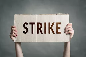 A PAIR OF HANDS HOLDS A SIGN HORIZONTALLY THAT READS "STRIKE."