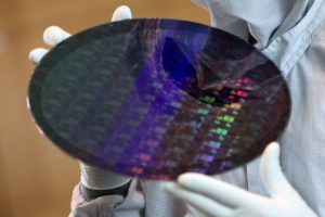 A PAIR OF HANDS WEARING WHITE GLOVES IS HOLDING A MULTI-COLORED SILICON WAFER.