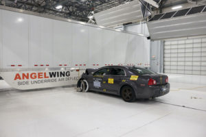 A BLACK CAR HAS COMPLETED A CRASH TEST INTO A TRAILER THAT HAS A SIDE UNDERRIDE GUARD. THE FRONT OF THE CAR IS SLIGHTLY DAMAGED.