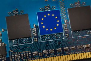 THE EU FLAG IS PRINTED ON A CHIP IN THE CENTER OF A CIRCUIT BOARD SURROUNDED BY A PAIR OF UNMARKED BLACK CHIPS.