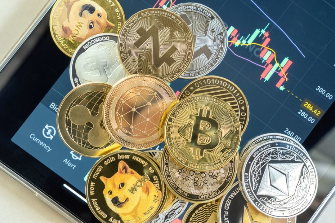 A GRAPHIC SHOWS MULTIPLE TYPES OF CRYPTO CURRENCIES REPRESENTED IN THE FORM OF COINS, CROWDING OUT THE SCREEN OF A SMARTPHONE