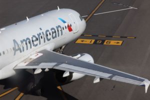 A WHITE AMERICAN AIRLINES-LABELED AIRCRAFT SITS ON A RUNWAY.