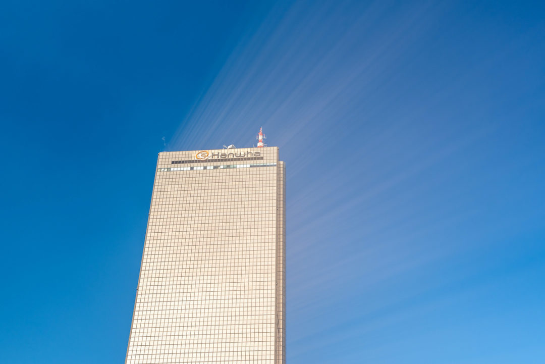 SUNLIGHT REFLECTS OFF THE GOLD-TINTED GLASS OF A HANWHA SKYSCRAPER.