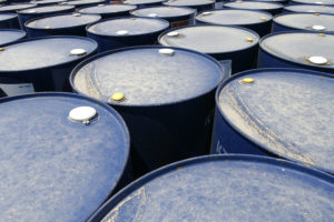 SEVERAL BLUE BARRELS OF OIL CAN BE SEEN HUDDLED TOGETHER.