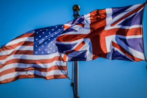 THE U.S. AND U.K. FLAGS ARE FLAPPING IN THE WIND NEXT TO EACH OTHER ON TWO DIFFERENT POLES.