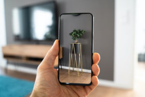 A CELL PHONE AUGMENTED REALITY APPLICATION SHOWS A GOLD AND BLACK STAND AGAINST A WALL WITH A PLANT ON TOP OF IT.