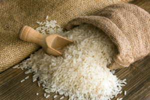 UNCOOKED WHITE RICE AND A WOODEN SCOOP IS SPILLING OUT OF A BROWN BURLAP SACK.