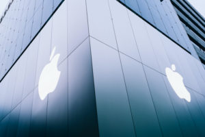 THE OUTSIDE CORNER OF A GLASS BUILDING HAS APPLE LOGOS ON BOTH SIDES OF IT.