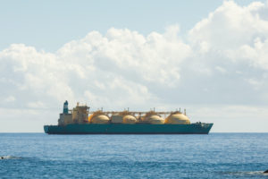A LIQUIFIED NATURAL GAS CARRIER SITS ON A BODY OF WATER BELOW A BLUE AND SOMEWHAT CLOUDY SKY.