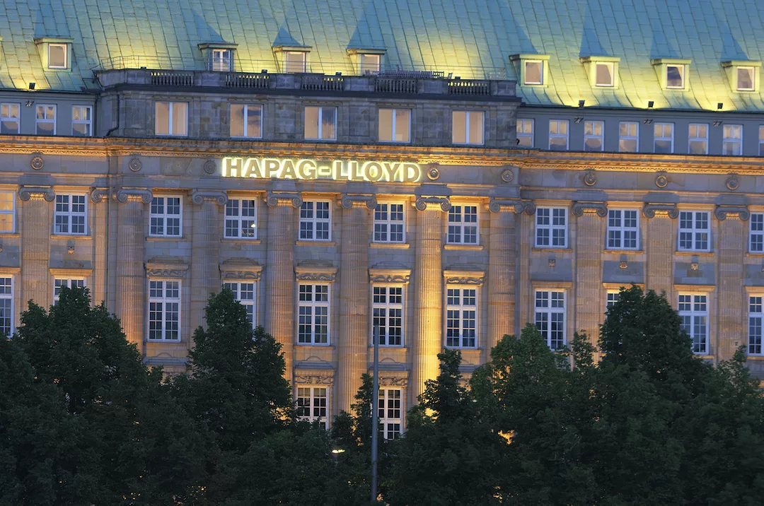 THE EXTERIOR OF A BUILDING THAT HAS THE HAPAG-LLOYD LOGO ON IT CAN BE SEEN AT NIGHT.