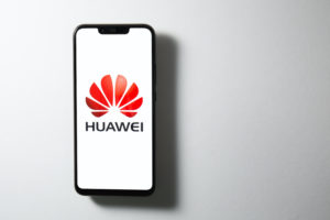 THE HUAWEI LOGO CAN BE SEEN ON A SMARTPHONE SCREEN IN FRONT OF A GREY BACKGROUND.