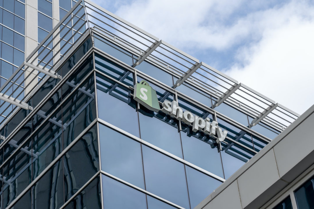 A SHOPIFY SIGN CAN BE SEEN ON A GLASS BUILDING UNDERNEATH A CLOUDY BLUE SKY.