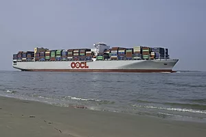 A LARGE CONTAINER SHIP TRAVELING NEAR THE SHORE HAS AN OOCL LOGO ON THE SIDE OF IT.