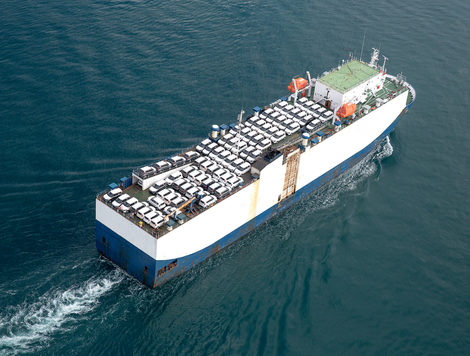 A TRANSPORT VESSEL CAN BE SEEN SAILING ON THE OCEAN WHILE CARRYING SEVERAL VEHICLES.