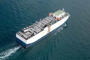 A TRANSPORT VESSEL CAN BE SEEN SAILING ON THE OCEAN WHILE CARRYING SEVERAL VEHICLES.