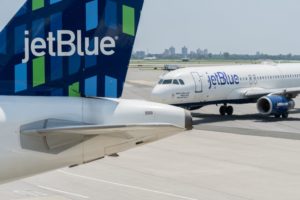 THE RUDDER AND THE FRONT HALF OF A DIFFERENT JETBLUE AIRCRAFT CAN BE SEEN ON AN AIRPORT RUNWAY.