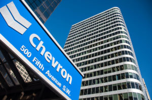 A GROUND VIEW LOOKING UP AT A CHEVRON SIGN NEXT TO A SKYSCRAPER.