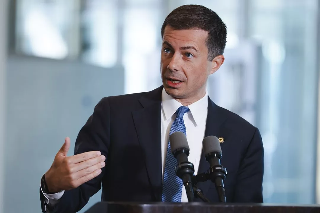 A MAN IN A SUIT AND TIE GESTURES WHILE SPEAKING AT A PODIUM WITH TWO MICROPHONES