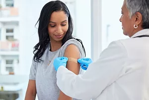 A DOCTOR PLACES A BAND AID ON THE SHOULDER OF A PATIENT.
