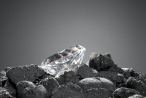 A DIAMOND SITS ON TOP OF A PILE OF COAL IN FRONT OF A GREY BACKGROUND.